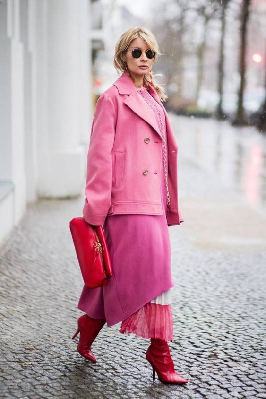 un look super audacieux avec une robe rose, une jupe rose et blanche, des bottes rouges, un manteau court rose vif et un sac rouge