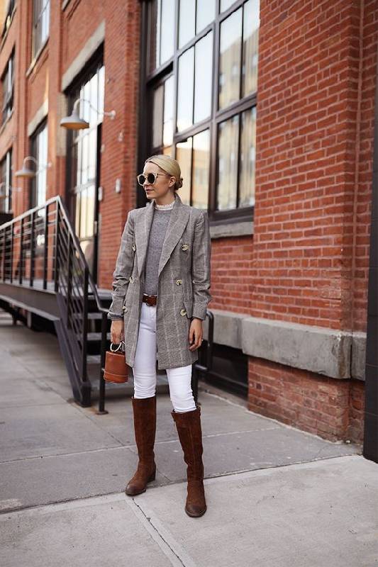 une tenue preppy avec un haut gris, un blazer gris à carreaux, des skinnies blancs, des bottes marron et un sac à seaux marron